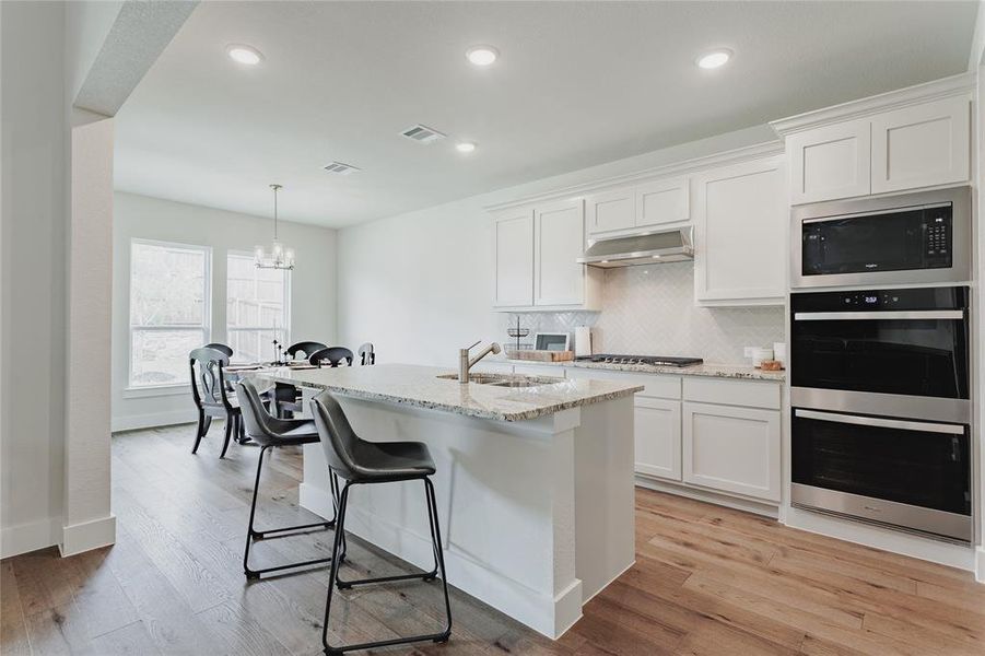 Kitchen featuring a large island with a sink, stainless steel appliances, white cabinetry, wood-finish flooring, and recessed lighting
