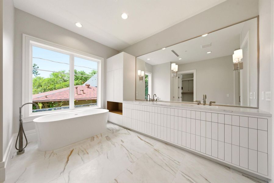 Luxurious spa primary bath with freestanding soaking tub, dual vanity, and oversized picture window. Luxurious spa primary bath with freestanding soaking tub, dual vanity, and oversized picture window.