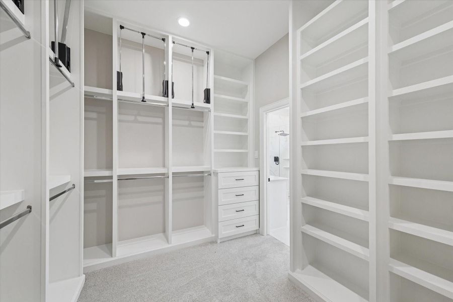 Second view of the primary closet showing open shelving and drawer storage.  Also, pull down hanging bars for easier access.