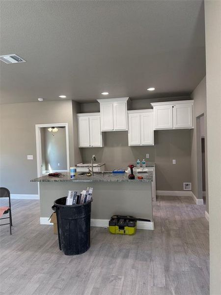 Kitchen featuring light stone countertops, a kitchen island with sink, light wood-type flooring, white cabinets, and recessed lighting Kitchen featuring light stone countertops, a kitchen island with sink, light wood-type flooring, white cabinets, and recessed lighting