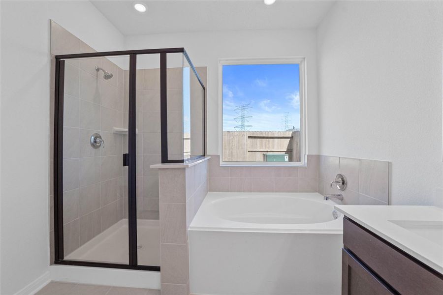 This additional view of the primary bath highlights a dark framed walk-in shower with elegant tile surround, a separate garden tub ideal for relaxing after a long day, and a large window that offers plenty of natural light!