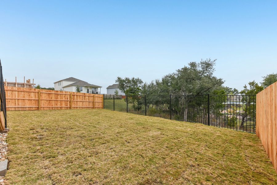 A fenced in yard with a tree and a house in the background. A fenced in yard with a tree and a house in the background.