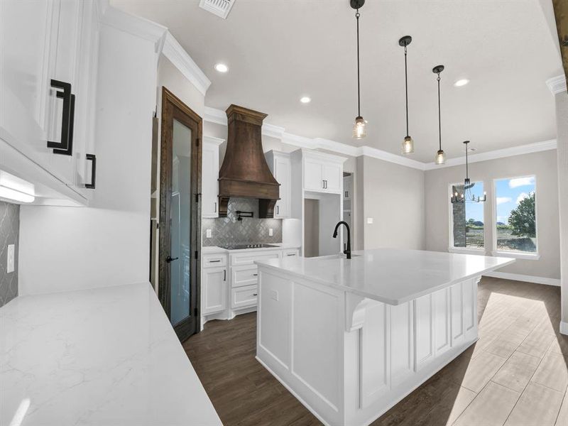 Kitchen featuring custom range hood, a kitchen island with sink, dark hardwood / wood-style floors, hanging light fixtures, and decorative backsplash