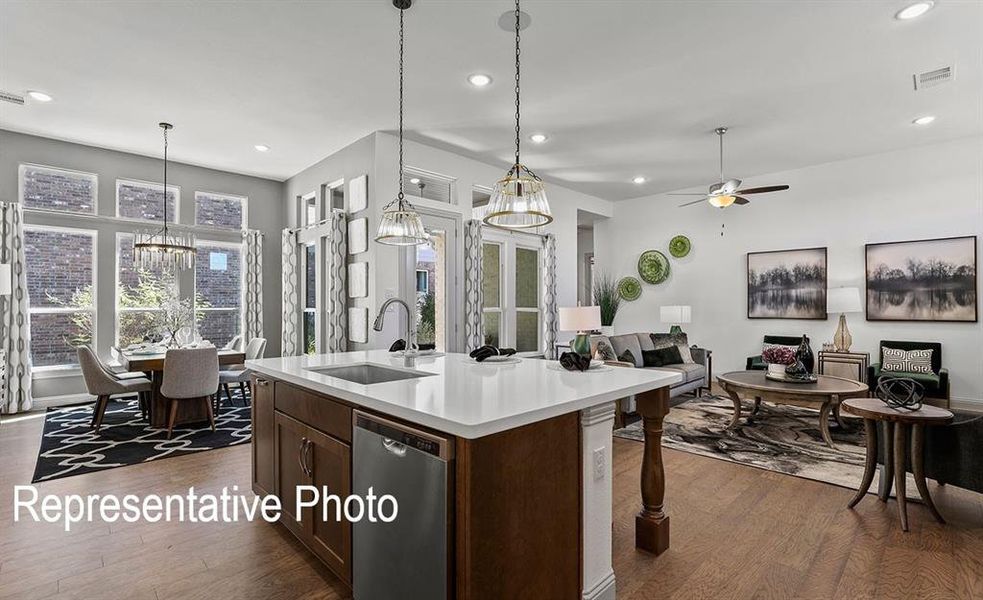 Open-concept living space featuring wood-finish flooring, a kitchen island with a white countertop and integrated sink, stainless steel appliances, and abundant natural light from large windows Open-concept living space featuring wood-finish flooring, a kitchen island with a white countertop and integrated sink, stainless steel appliances, and abundant natural light from large windows