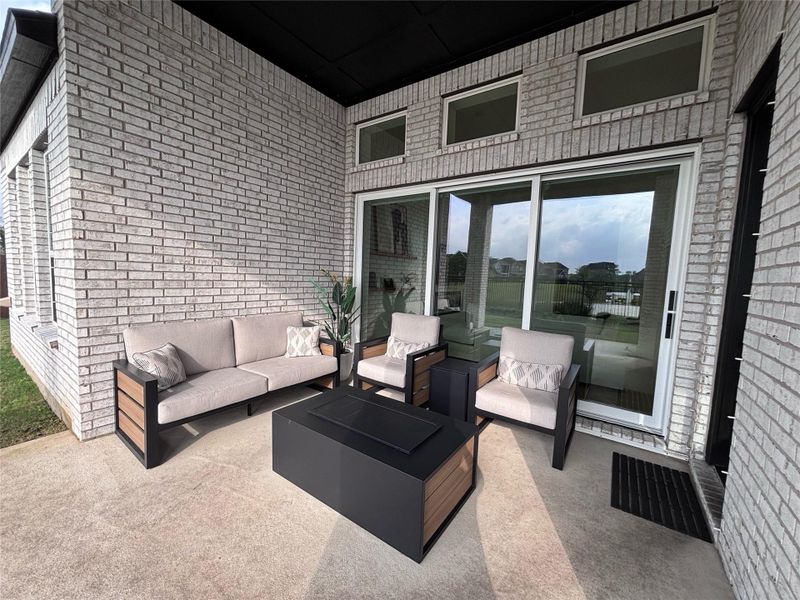 The spacious covered patio features modern outdoor seating, a ceiling fan with large windows offering scenic views of a nearby lake. Perfect for relaxing and entertaining.
