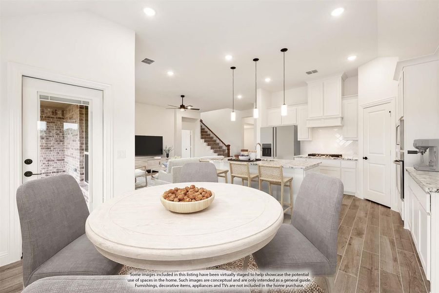 Open-plan dining area with round white table, leading to kitchen with white cabinets and island, and living room beyond.
