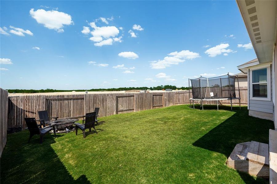 Fenced backyard featuring a trampoline and an outdoor fire pit