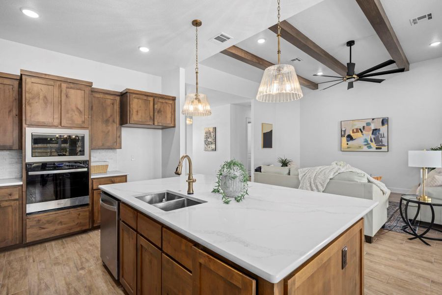 Kitchen with open floor plan, oven, light wood-style floors, a center island with sink, and beamed ceiling