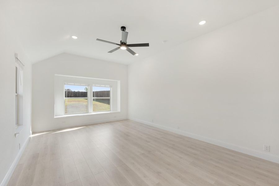 Empty room with vaulted ceiling, ceiling fan, light wood floors, and a backyard-facing window
