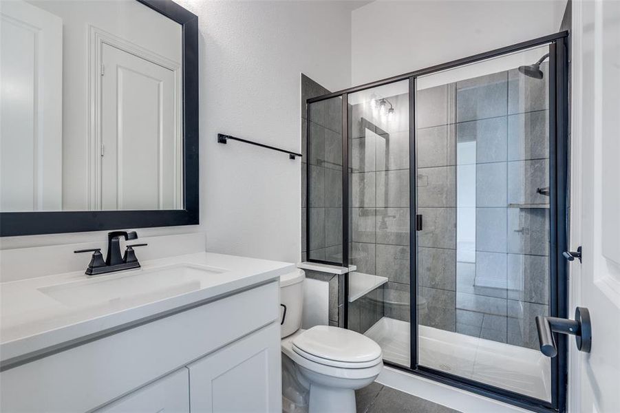 Bathroom featuring a shower with door, tile flooring, vanity, and toilet