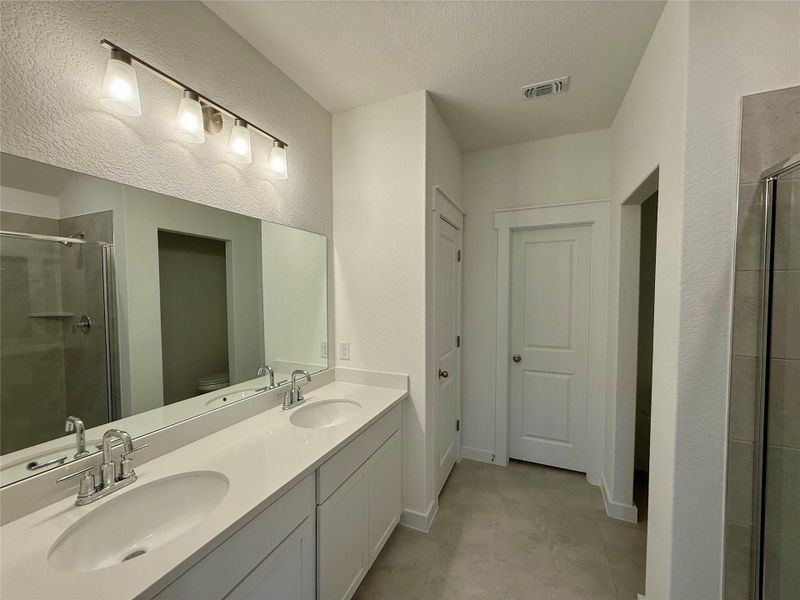 Bathroom featuring a shower stall, double vanity, a textured wall, a textured ceiling, and light tile patterned floors Bathroom featuring a shower stall, double vanity, a textured wall, a textured ceiling, and light tile patterned floors