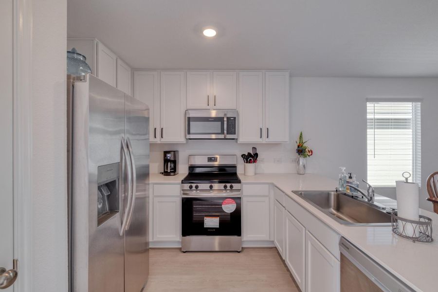 The kitchen features white cabinetry, stainless steel appliances, and light-colored countertops