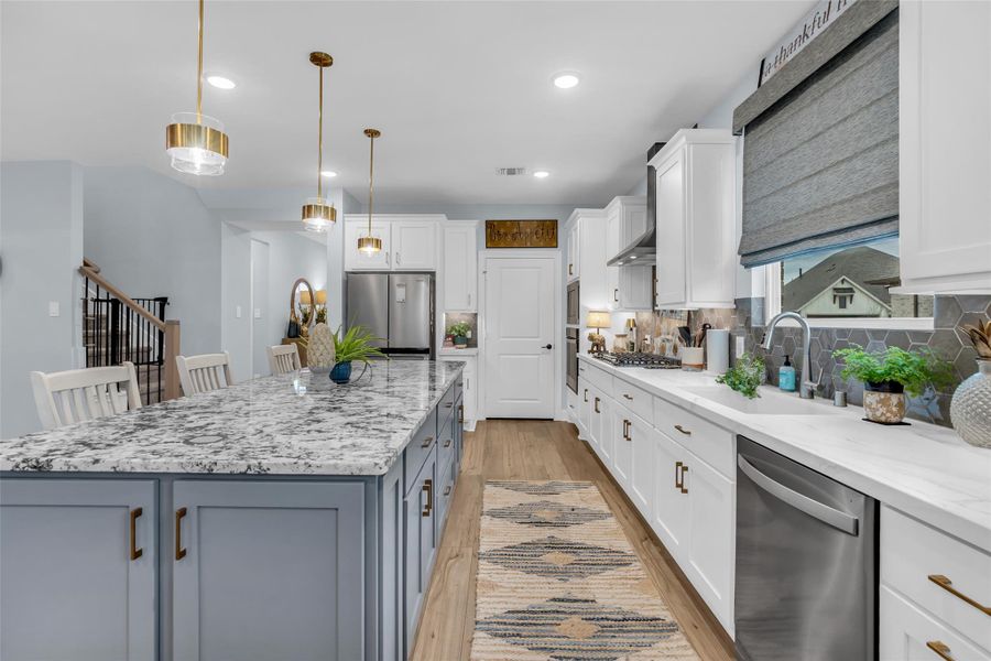 The kitchen features a massive island with granite countertop, dual toned cabinetry, quartz counter, stainless appliances, and bronze fixtures. The kitchen features a massive island with granite countertop, dual toned cabinetry, quartz counter, stainless appliances, and bronze fixtures.