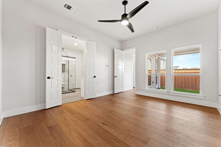 Unfurnished bedroom with ensuite bathroom, ceiling fan, and light wood-type flooring