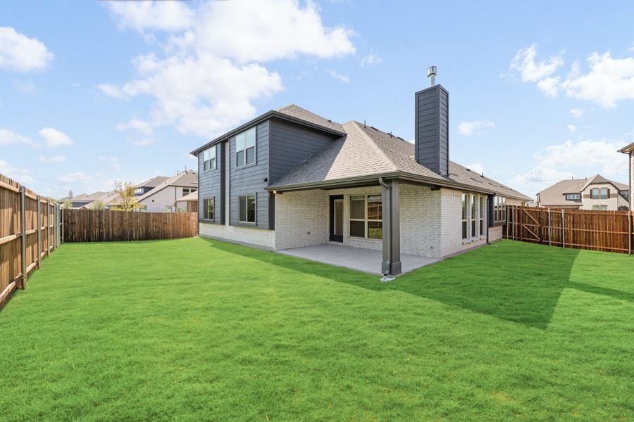 Backyard of two-story home with brick exterior, covered patio, and fenced green lawn