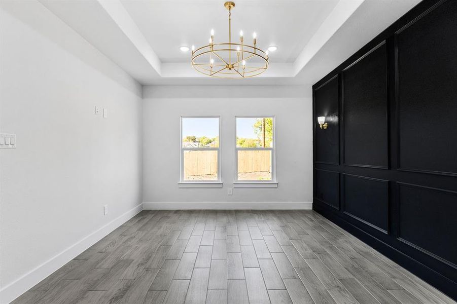 Empty room featuring a tray ceiling, light wood-type flooring, and an inviting chandelier