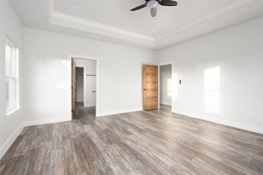 Unfurnished bedroom featuring wood finished floors, ceiling fan, a tray ceiling, and ornamental molding