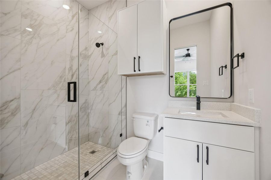 Full-height tilework and modern black fixtures create contrast within the design of the bath. The walk-in shower and quartz surfaces continue the home’s consistent finish palette throughout. Full-height tilework and modern black fixtures create contrast within the design of the bath. The walk-in shower and quartz surfaces continue the home’s consistent finish palette throughout.