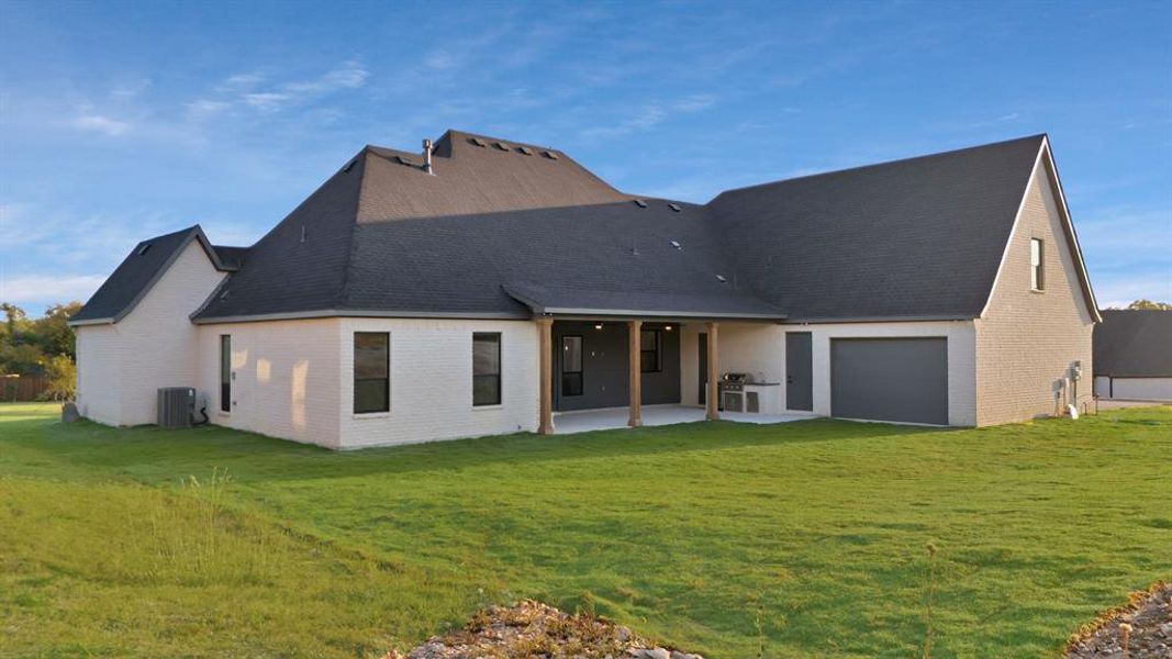 Back of house featuring a yard, a patio, central AC unit, and a garage