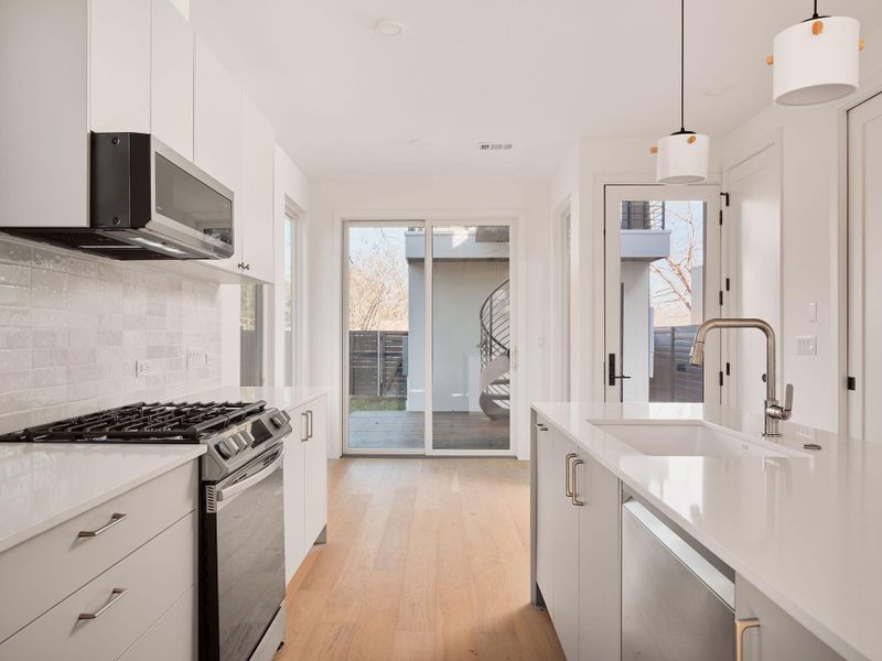 Kitchen with appliances with stainless steel finishes, modern cabinets, pendant lighting, decorative backsplash, and light wood-style flooring