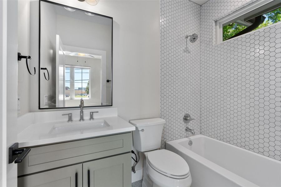 Full bathroom in the secondary bedroom. Featuring white quartz countertops, a white bathtub with a chrome showerhead, white hexagonal wall tiling, and a window Full bathroom in the secondary bedroom. Featuring white quartz countertops, a white bathtub with a chrome showerhead, white hexagonal wall tiling, and a window