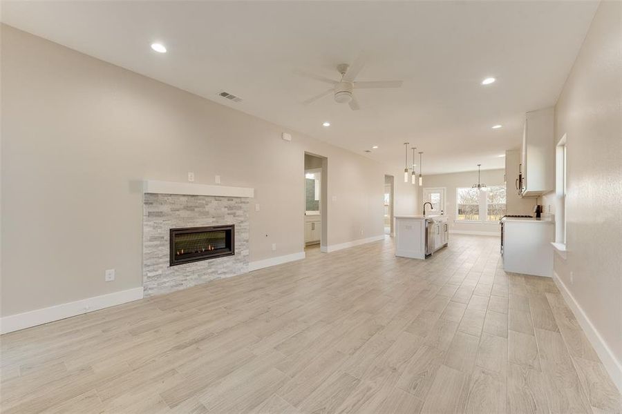 Unfurnished living room featuring sink, ceiling fan with notable chandelier, a fireplace, and light wood-type flooring