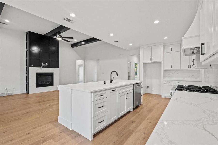 Kitchen featuring light stone counters, a kitchen island with sink, open floor plan, light wood-type flooring, and white cabinetry