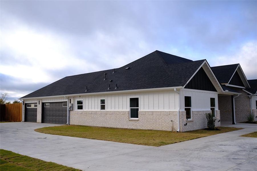 View of side of property with board and batten siding, concrete driveway, a garage, a yard, and brick siding