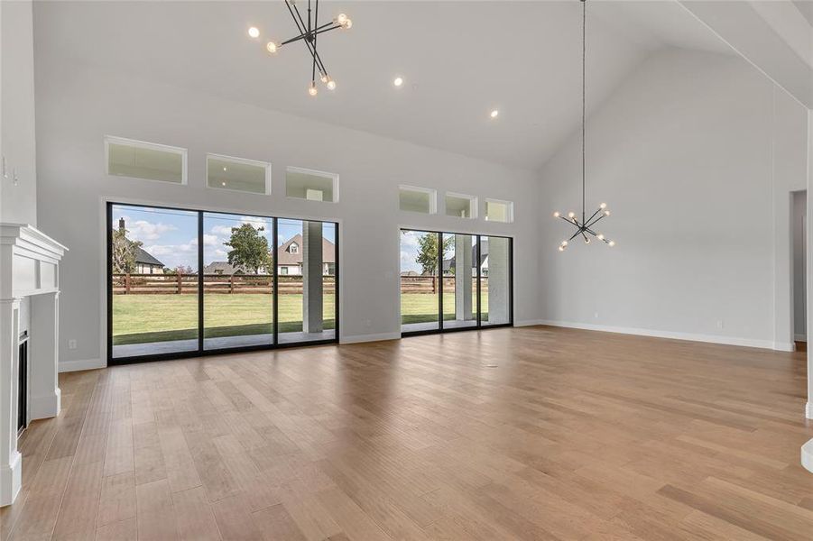 Unfurnished living room featuring a notable chandelier, light hardwood / wood-style flooring, and high vaulted ceiling