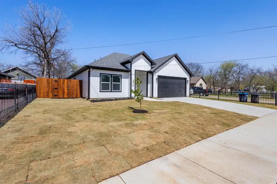 Modern inspired farmhouse featuring an attached garage, concrete driveway, roof with shingles, and fence