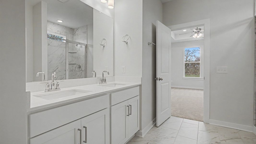 Beautiful and clean white bathroom with quartz countertops and marble-style tile flooring and shower walls