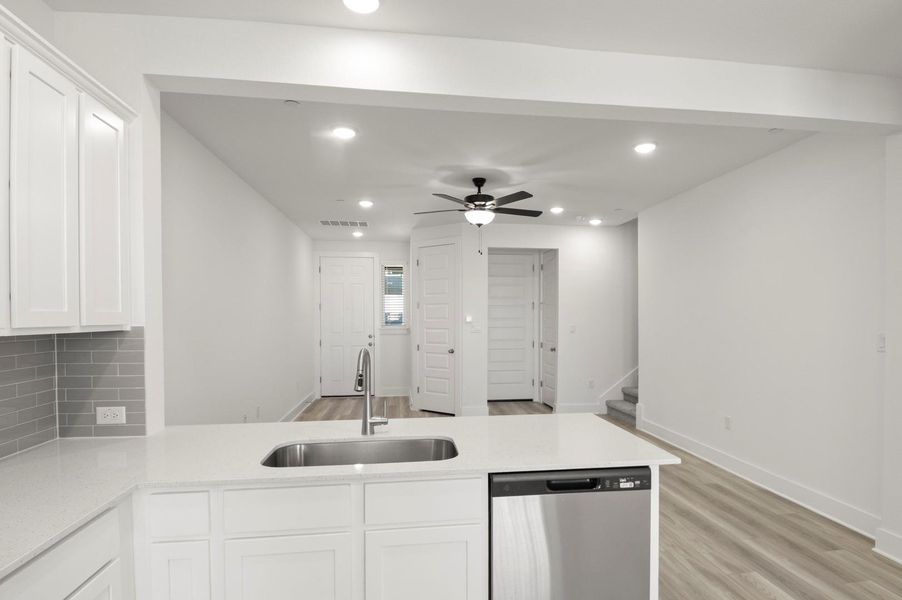 Kitchen featuring dishwasher, white cabinets, light stone countertops, ceiling fan, and a peninsula