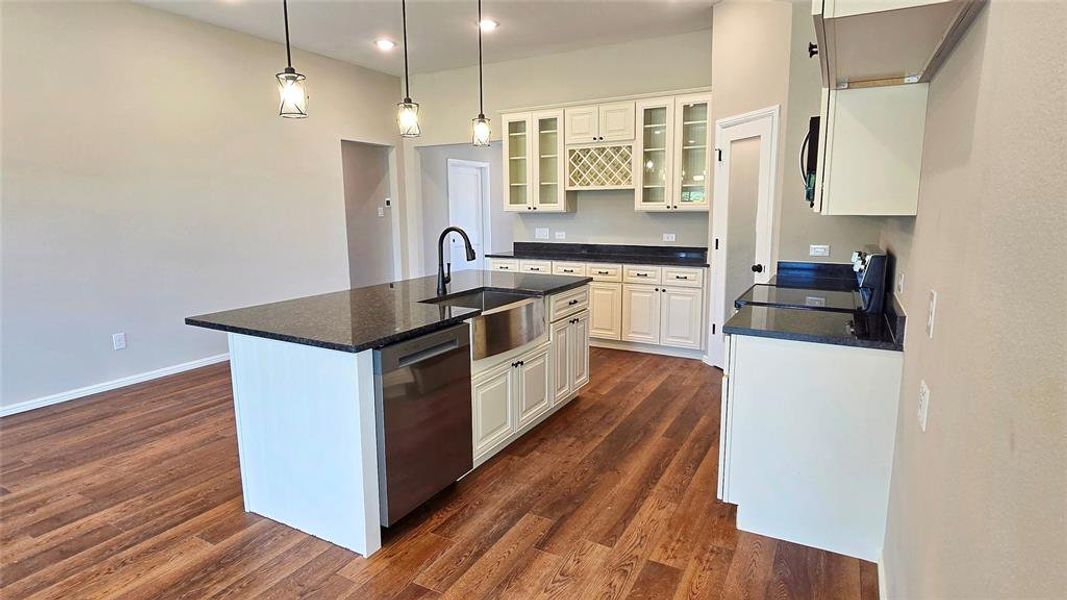 Kitchen with recessed lighting, stainless steel dishwasher, white cabinetry, dark wood-type flooring, and an island with sink