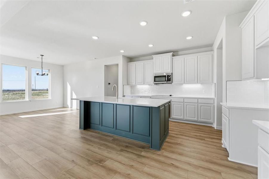 Kitchen featuring white cabinets, a center island with sink, backsplash, recessed lighting, and stainless steel microwave