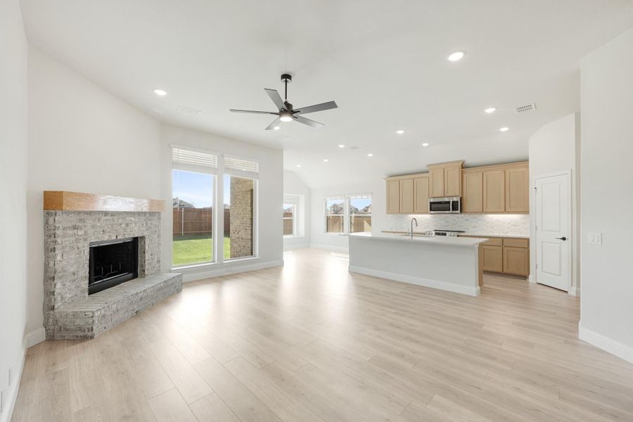 Open-concept living area with brick fireplace, ceiling fan, and kitchen with island and light wood cabinets