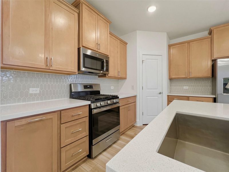 Kitchen featuring stainless steel appliances, decorative backsplash, light wood-type flooring, light stone countertops, and light wood finish cabinetry