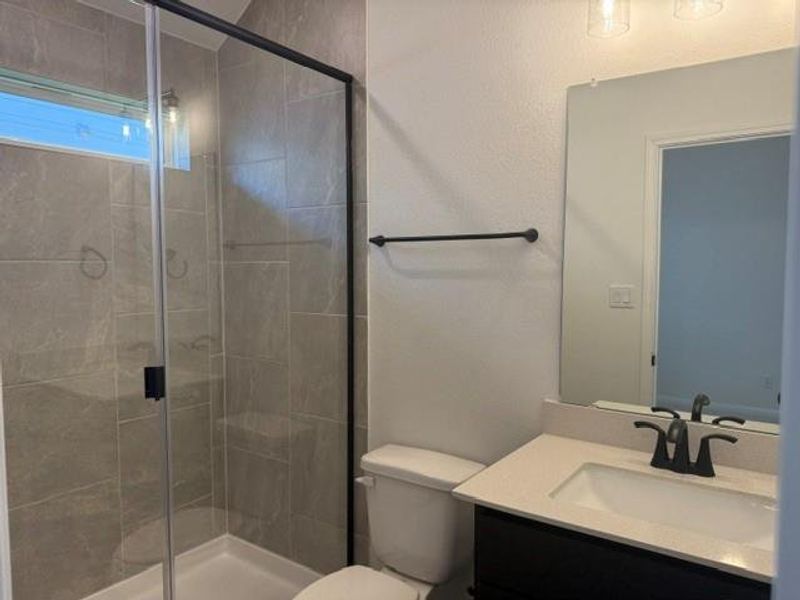 Bathroom with a glass-enclosed shower, dark vanity with light countertop, and a rectangular mirror