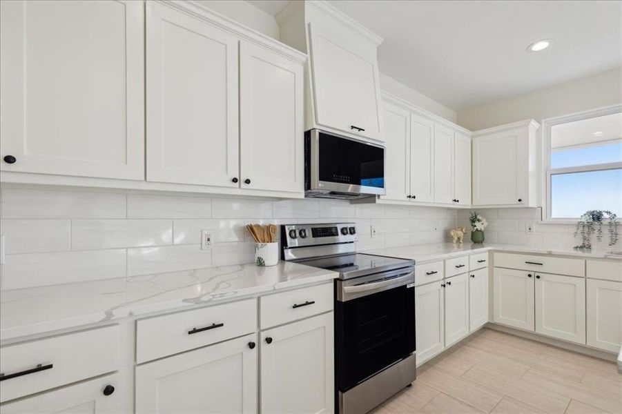 Kitchen featuring stainless steel appliances, light stone counters, white cabinetry, and tasteful backsplash