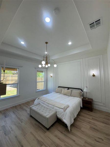 Bedroom with a raised ceiling, light wood-style floors, and recessed lighting