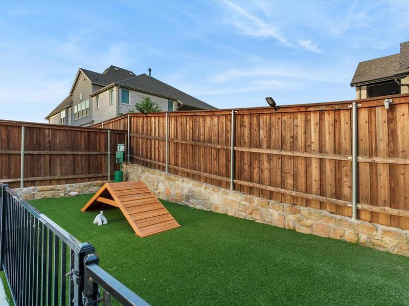Dedicated pet area featuring artificial turf, a wood ramp, and a black wrought iron fence Dedicated pet area featuring artificial turf, a wood ramp, and a black wrought iron fence