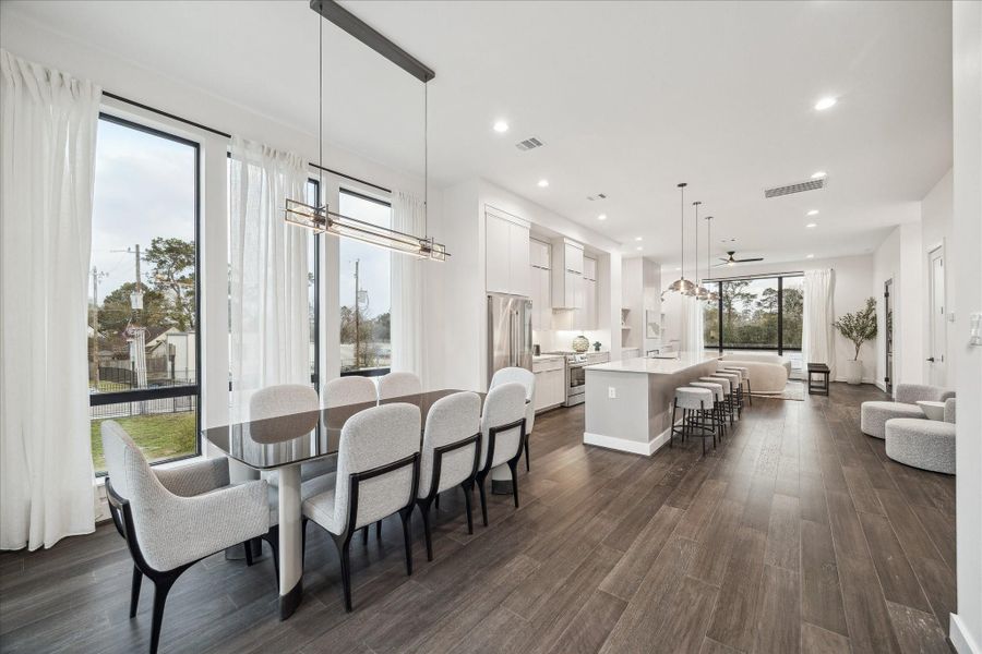 Bright, airy main level highlighting uninterrupted flow from dining to kitchen to living area. Walls of windows flood the interior with light, accentuating the clean white palette and rich flooring tones. Recessed lighting and elevated ceiling heights create a spacious ambiance ideal for entertaining, while the balanced proportions and modern lines reflect contemporary design at its finest.