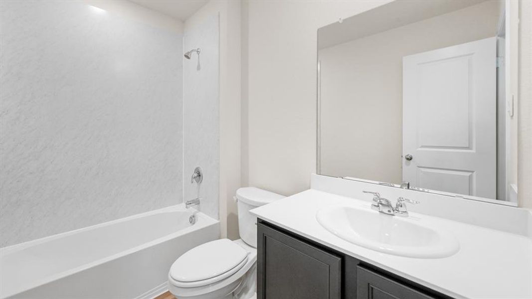 Bathroom featuring a white tub with shower, chrome fixtures, dark wood-finish vanity, white countertop with integrated sink, and an expansive mirror