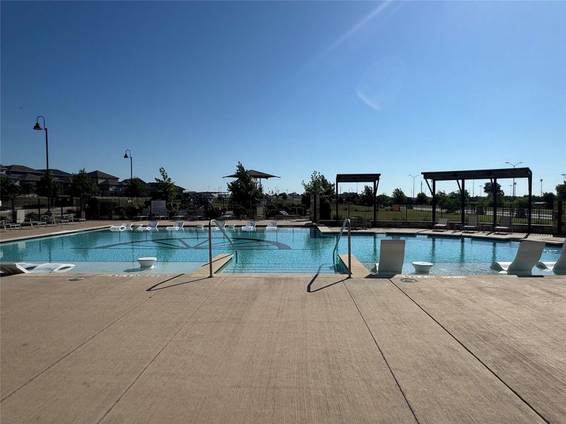 Expansive community pool featuring a concrete deck, integrated sun shelves, and decorative pergolas