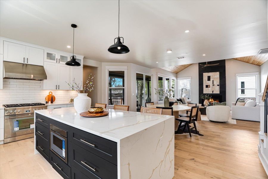 Open concept living space featuring a kitchen island with a white quartz countertop, stainless steel appliances, and light wood flooring throughout Open concept living space featuring a kitchen island with a white quartz countertop, stainless steel appliances, and light wood flooring throughout