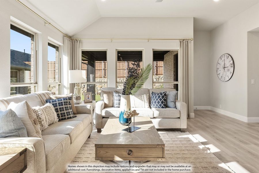 Living room with vaulted ceiling, light hardwood floors, neutral sofas, and large windows overlooking a backyard patio. Living room with vaulted ceiling, light hardwood floors, neutral sofas, and large windows overlooking a backyard patio.