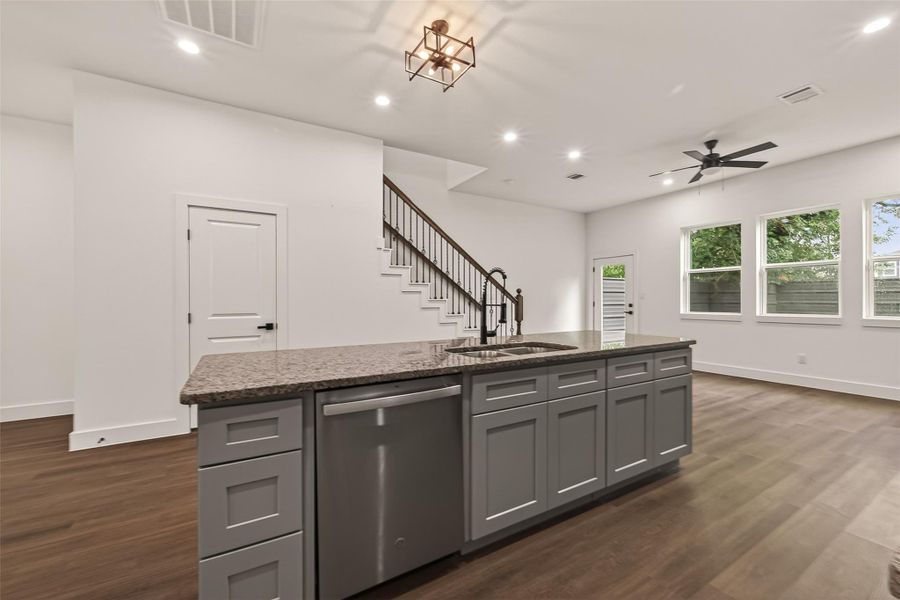 This spacious, open-concept living area features modern finishes with a large kitchen island, sleek cabinetry, and stainless steel appliances. The room is well-lit by natural light through multiple windows, and includes a stylish staircase and dark wood flooring. This spacious, open-concept living area features modern finishes with a large kitchen island, sleek cabinetry, and stainless steel appliances. The room is well-lit by natural light through multiple windows, and includes a stylish staircase and dark wood flooring.
