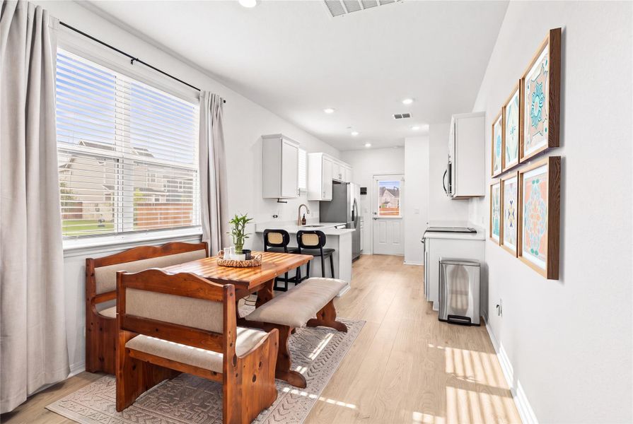 A naturally illuminated eat-in kitchen with sleek white cabinetry and light wood flooring.