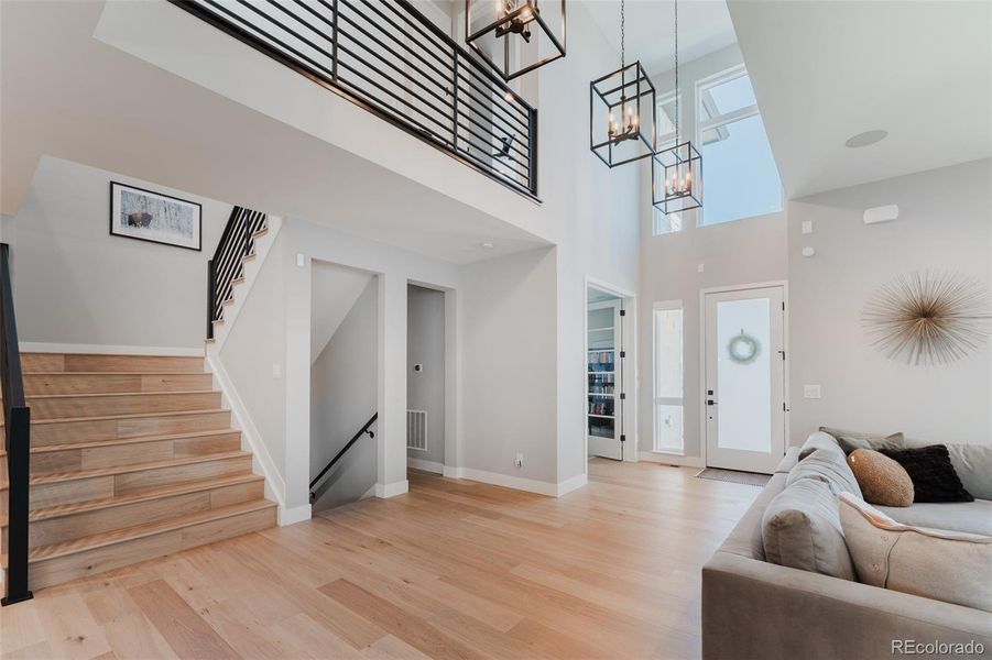 The upper level is elegantly framed by a sleek black steel railing, accompanied by strategically placed light fixtures that cast intriguing shadows, offering a dramatic introduction to the home's sophisticated interior design.