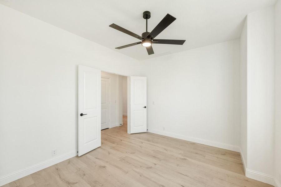 Empty bedroom with light wood floors, white walls, and a black ceiling fan with light fixture