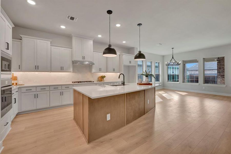 Dual tone kitchen with an island with sink, light wood-style flooring, hanging lights, stainless steel appliances, and dual tone cabinets
